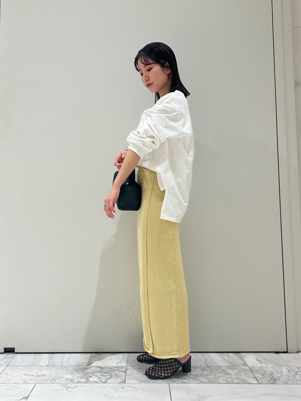 ブラック系のハンドバッグ、イエロー系のスカート、ホワイト系のTシャツ/カットソーを着用したレディースの春コーディネートの3枚目の写真