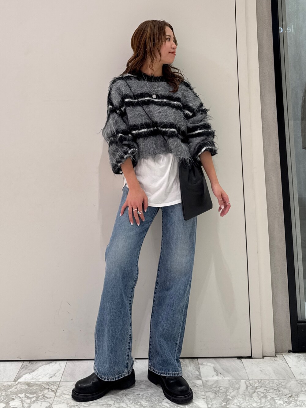 ブラック系のニット/セーター、ホワイト系のTシャツ/カットソー、ブルー系のデニムパンツを着用したレディースの冬コーディネートの7枚目の写真