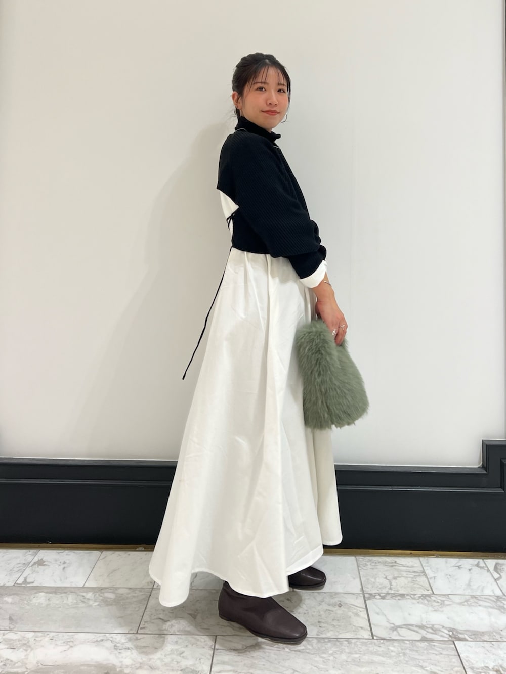 ブラック系のワンピース、グリーン系のハンドバッグ、ブラウン系のブーツを着用したレディースの冬コーディネートの4枚目の写真