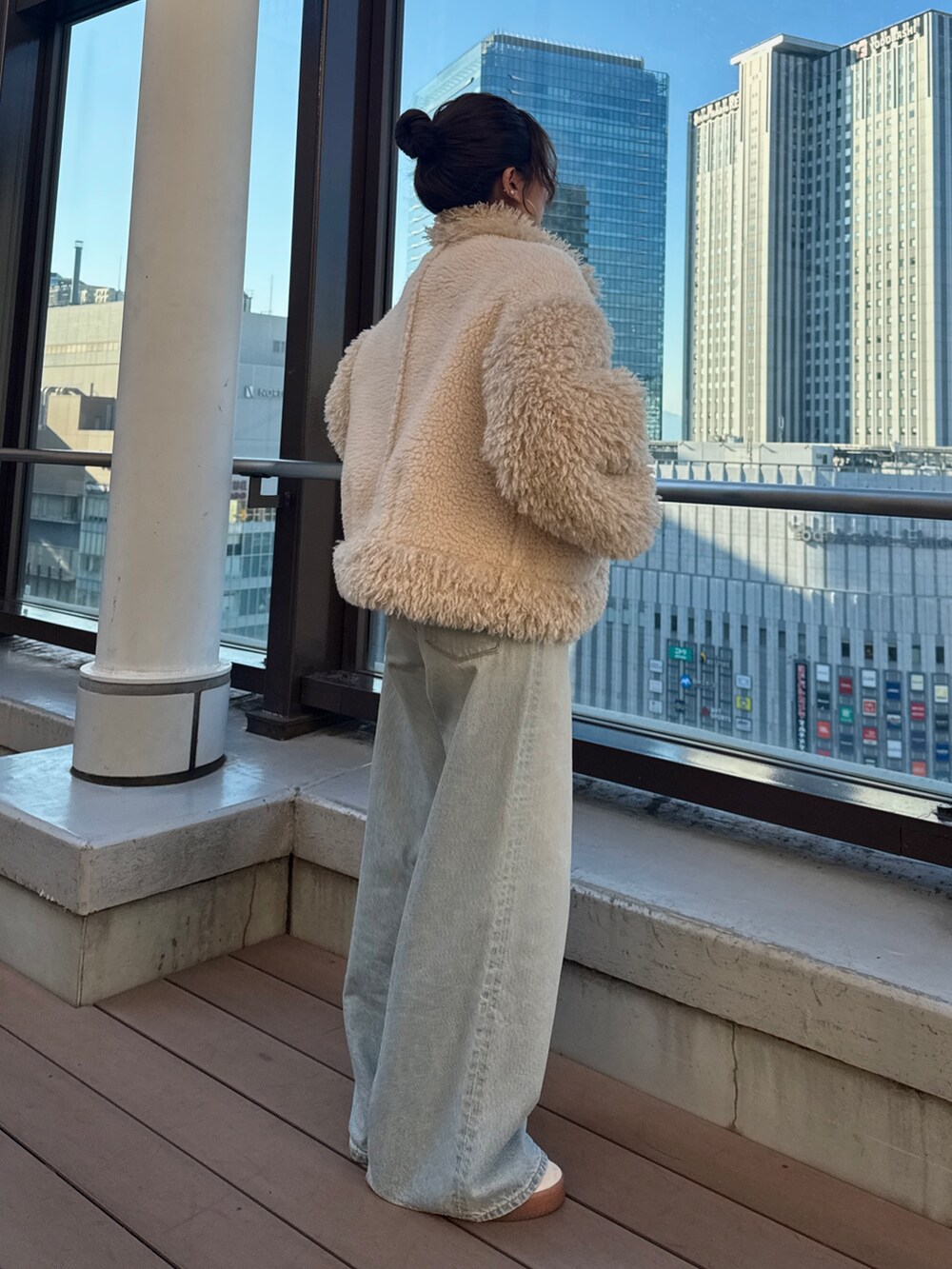 ホワイト系のムートンコート、グリーン系のニット/セーター、ブルー系のデニムパンツを着用したレディースの冬コーディネートの3枚目の写真