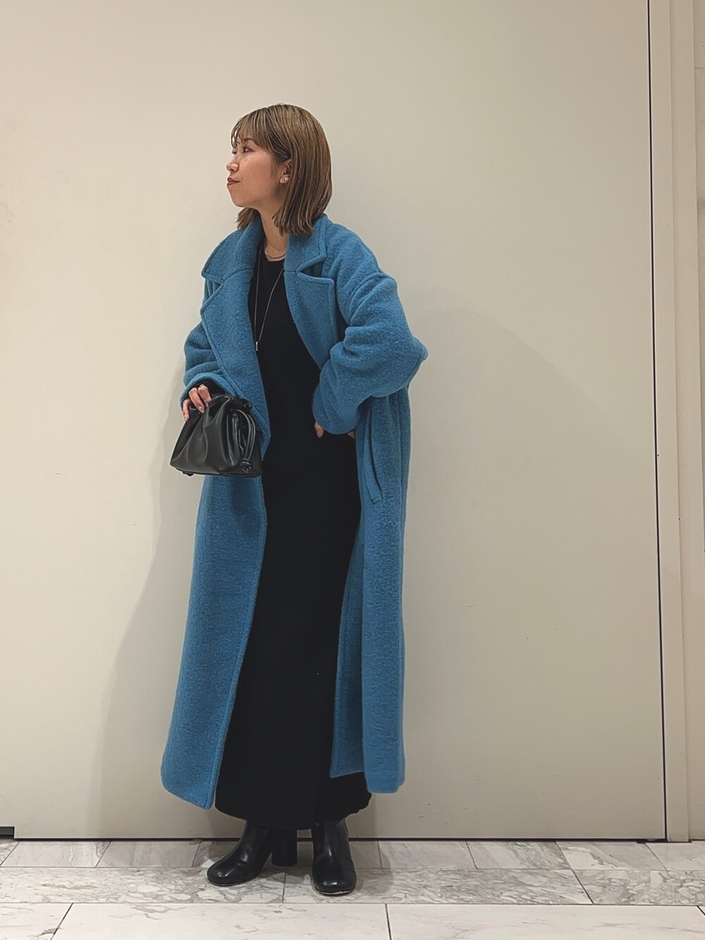 ブルー系のチェスターコート、ブラック系のワンピース、ブラック系のブーツを着用したレディースの冬コーディネートの4枚目の写真
