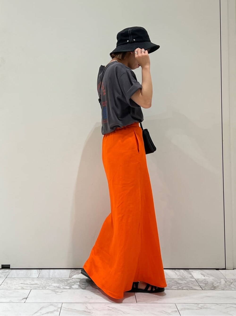 ブラック系のショルダーバッグ、グレー系のTシャツ/カットソー、オレンジ系のスカートを着用したレディースの夏コーディネートの4枚目の写真