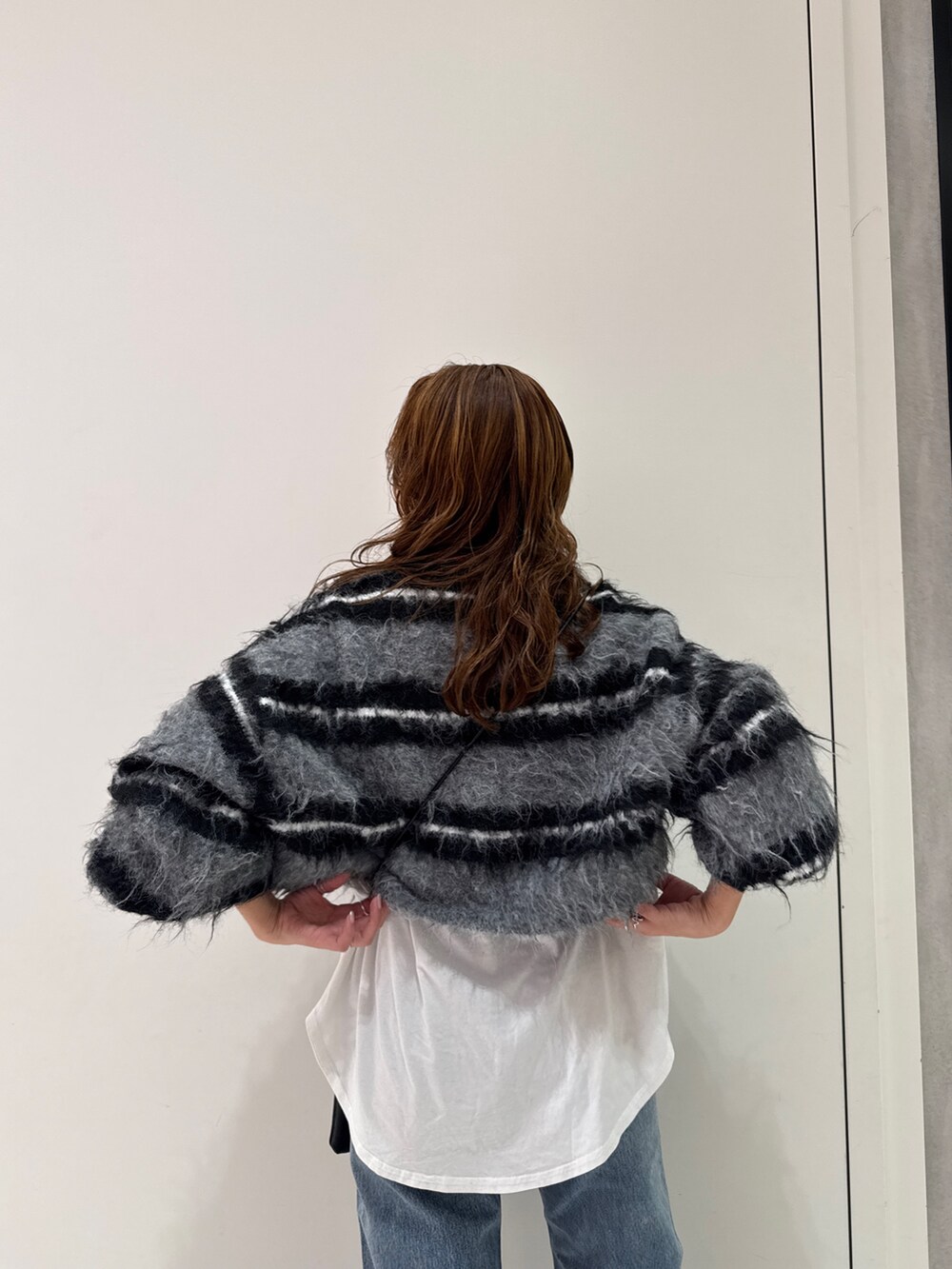 ブラック系のニット/セーター、ホワイト系のTシャツ/カットソー、ブルー系のデニムパンツを着用したレディースの冬コーディネートの10枚目の写真