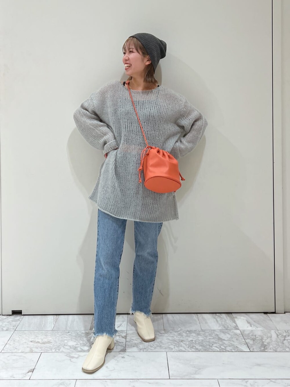 オレンジ系のハンドバッグ、ホワイト系のブーツ、ブルー系のデニムパンツを着用したレディースの秋コーディネートの6枚目の写真