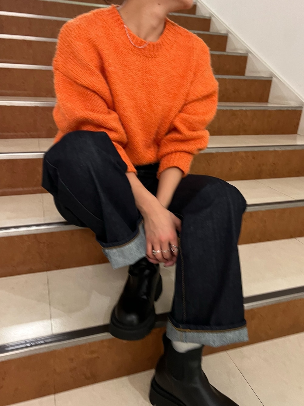 オレンジ系のニット/セーター、ブルー系のデニムパンツ、ホワイト系のダウンジャケット/コートを着用したレディースの秋コーディネートの9枚目の写真