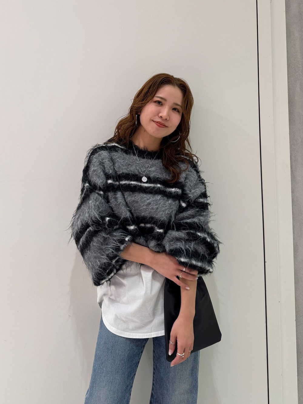 ブラック系のニット/セーター、ホワイト系のTシャツ/カットソー、ブルー系のデニムパンツを着用したレディースの冬コーディネートの8枚目の写真