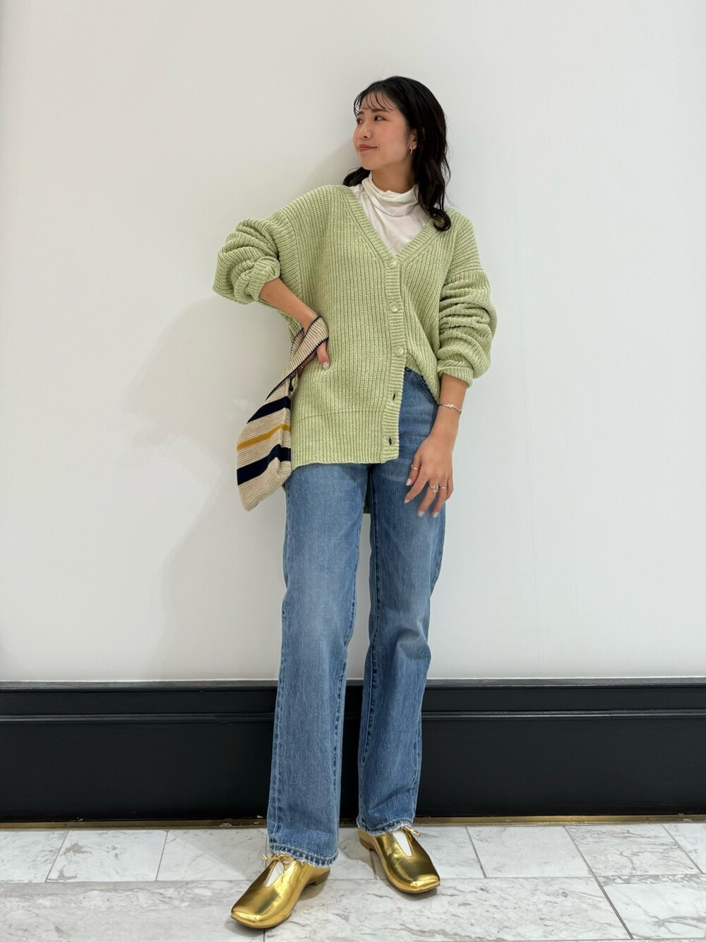 グリーン系のカーディガン/ボレロ、ホワイト系のハンドバッグ、ブルー系のデニムパンツを着用したレディースの冬コーディネートの2枚目の写真