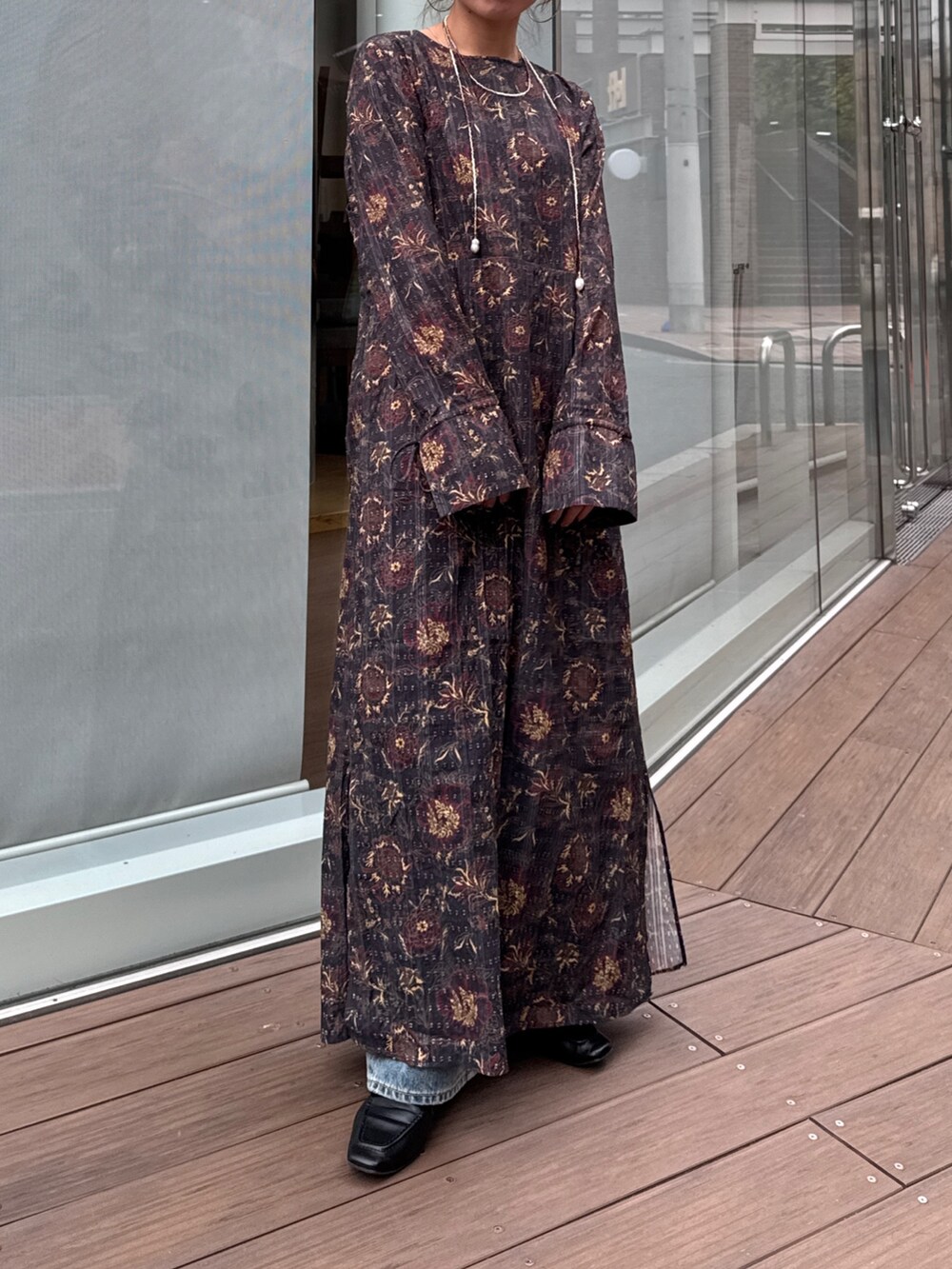 ブラック系のワンピース、ブルー系のデニムパンツ、ブラウン系のネックレスを着用したレディースの冬コーディネートの2枚目の写真