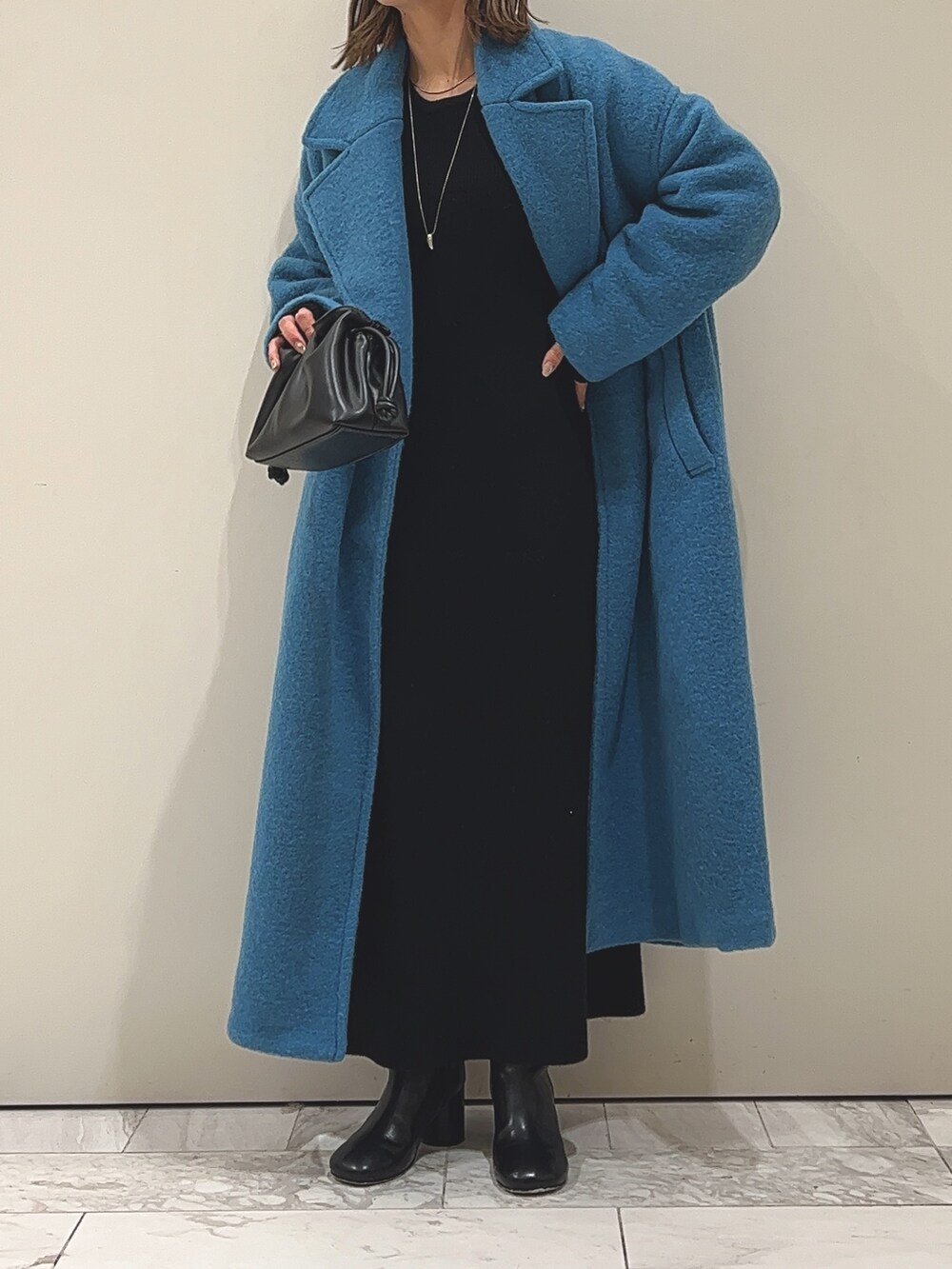 ブルー系のチェスターコート、ブラック系のワンピース、ブラック系のブーツを着用したレディースの冬コーディネートの5枚目の写真