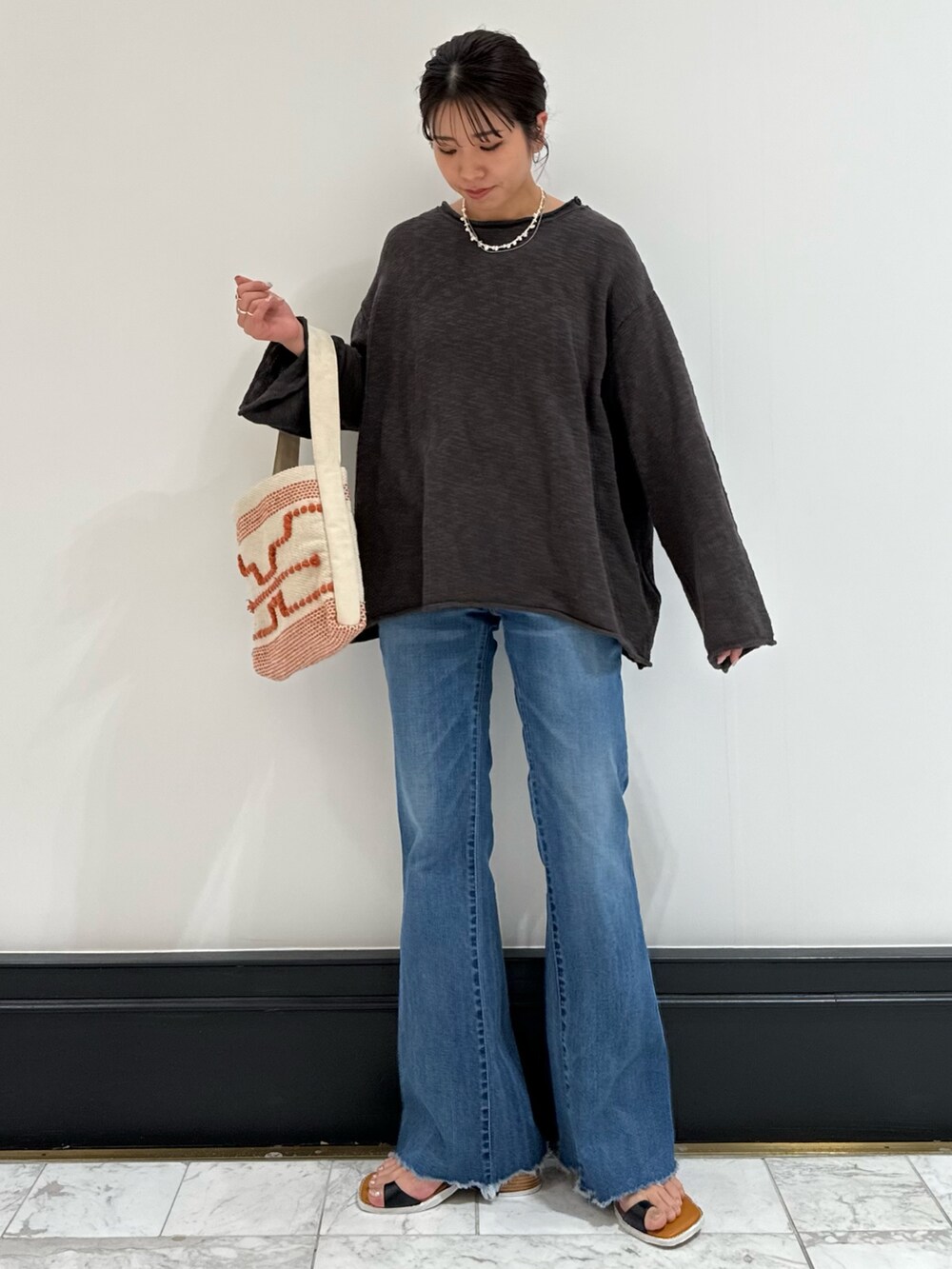 グレー系のニット/セーター、ブルー系のデニムパンツ、ブラック系のサンダルを着用したレディースの春コーディネートの2枚目の写真