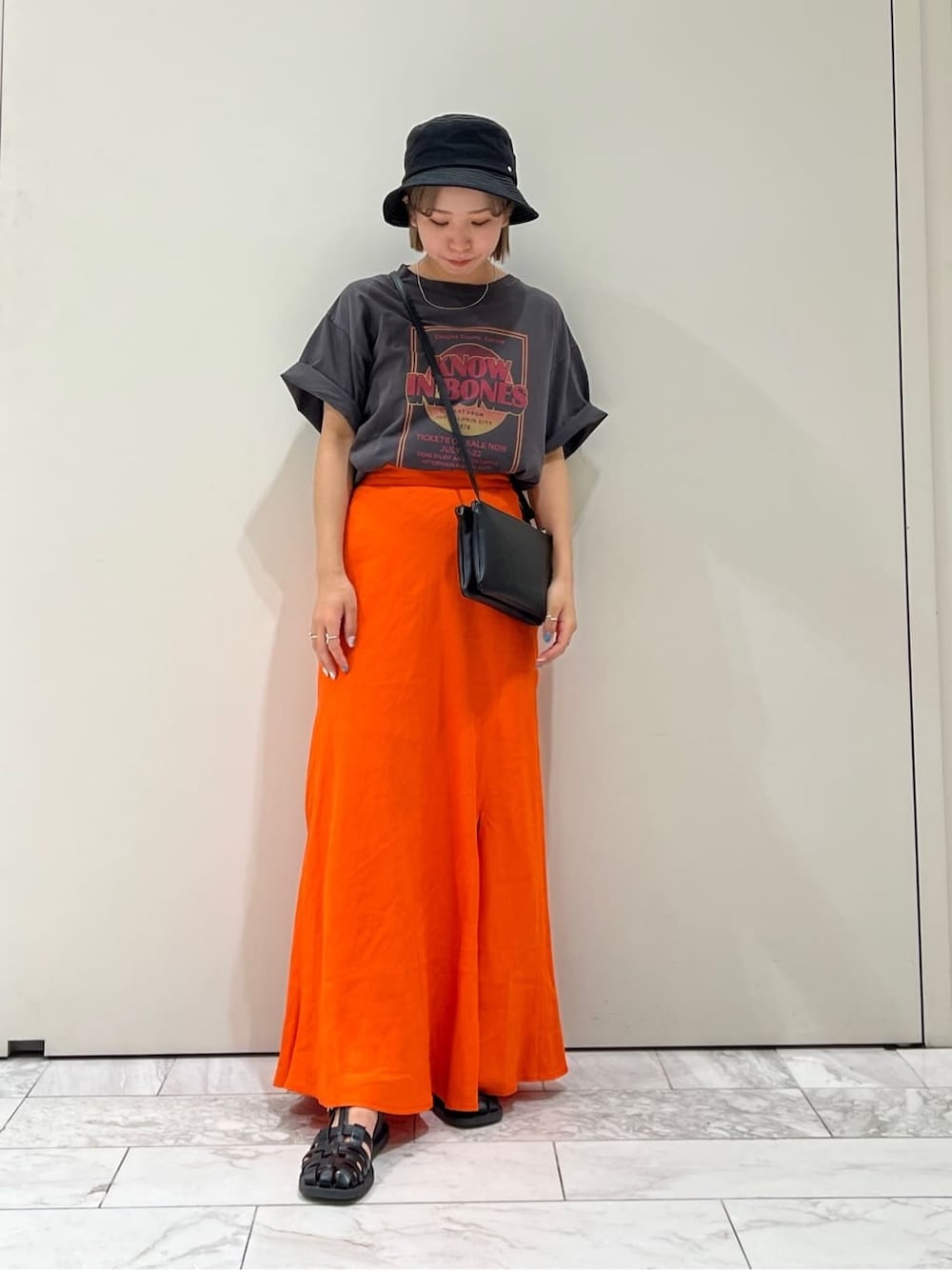 ブラック系のショルダーバッグ、グレー系のTシャツ/カットソー、オレンジ系のスカートを着用したレディースの夏コーディネートの8枚目の写真