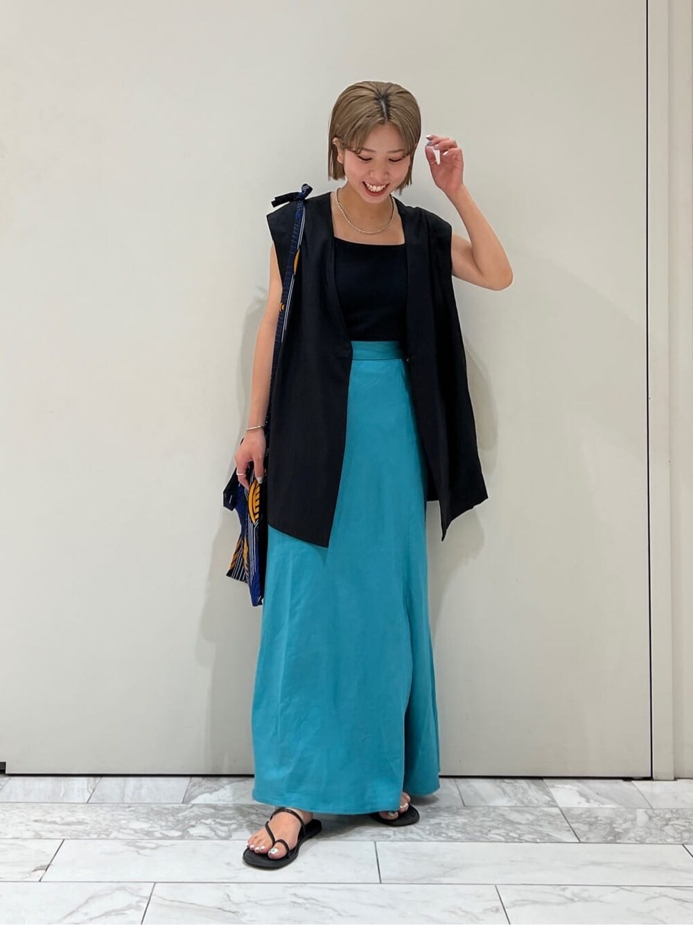 ブラック系のベスト、ブラック系のサンダル、ブルー系のスカートを着用したレディースの夏コーディネートの7枚目の写真