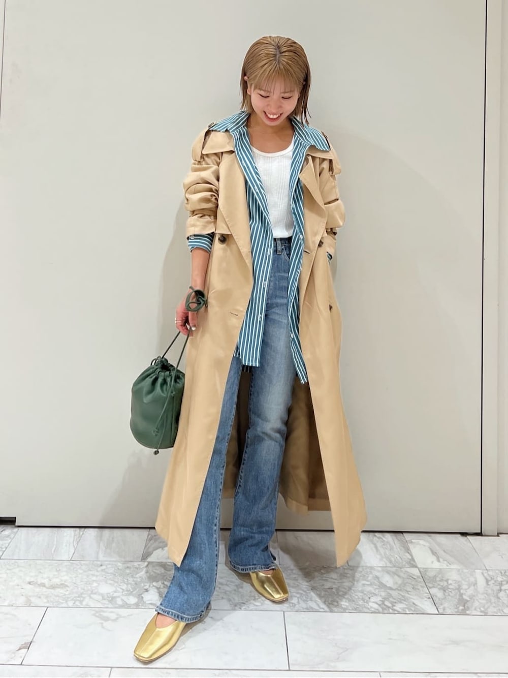 ベージュ系のトレンチコート、グリーン系のシャツ/ブラウス、ブルー系のデニムパンツを着用したレディースの夏コーディネートの3枚目の写真