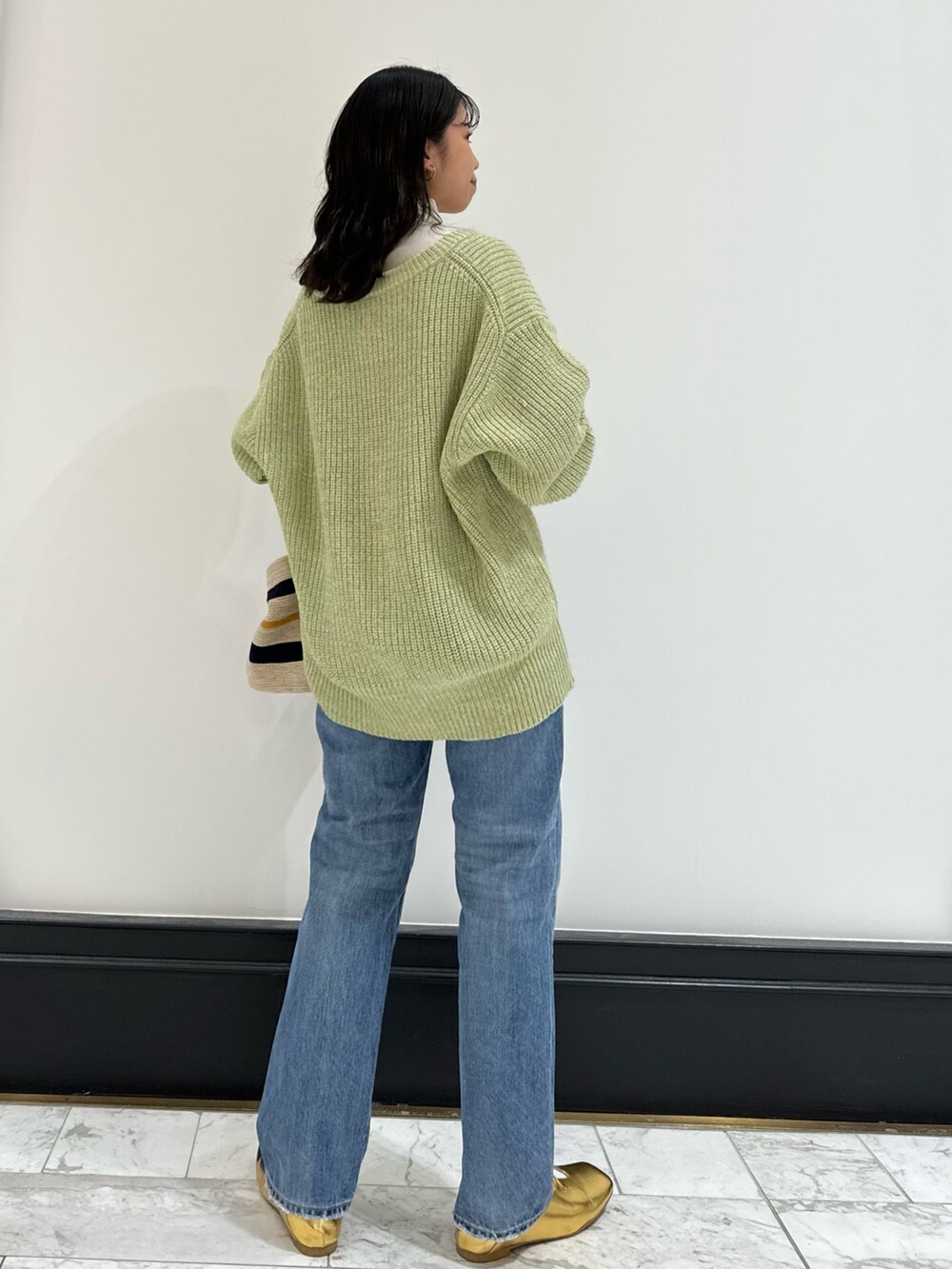 グリーン系のカーディガン/ボレロ、ホワイト系のハンドバッグ、ブルー系のデニムパンツを着用したレディースの冬コーディネートの4枚目の写真