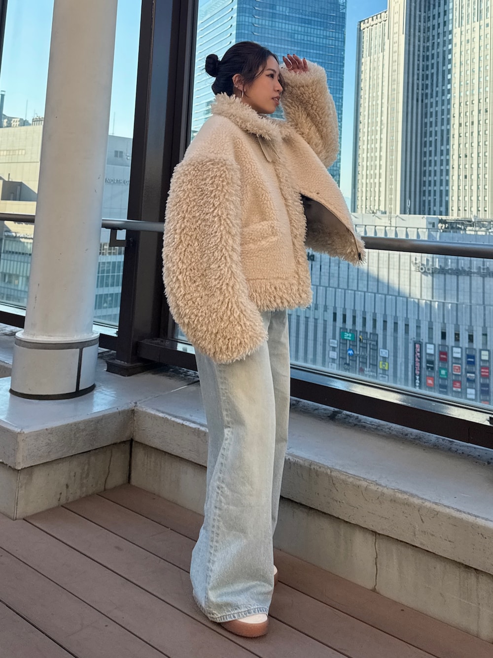 ホワイト系のムートンコート、グリーン系のニット/セーター、ブルー系のデニムパンツを着用したレディースの冬コーディネートの2枚目の写真