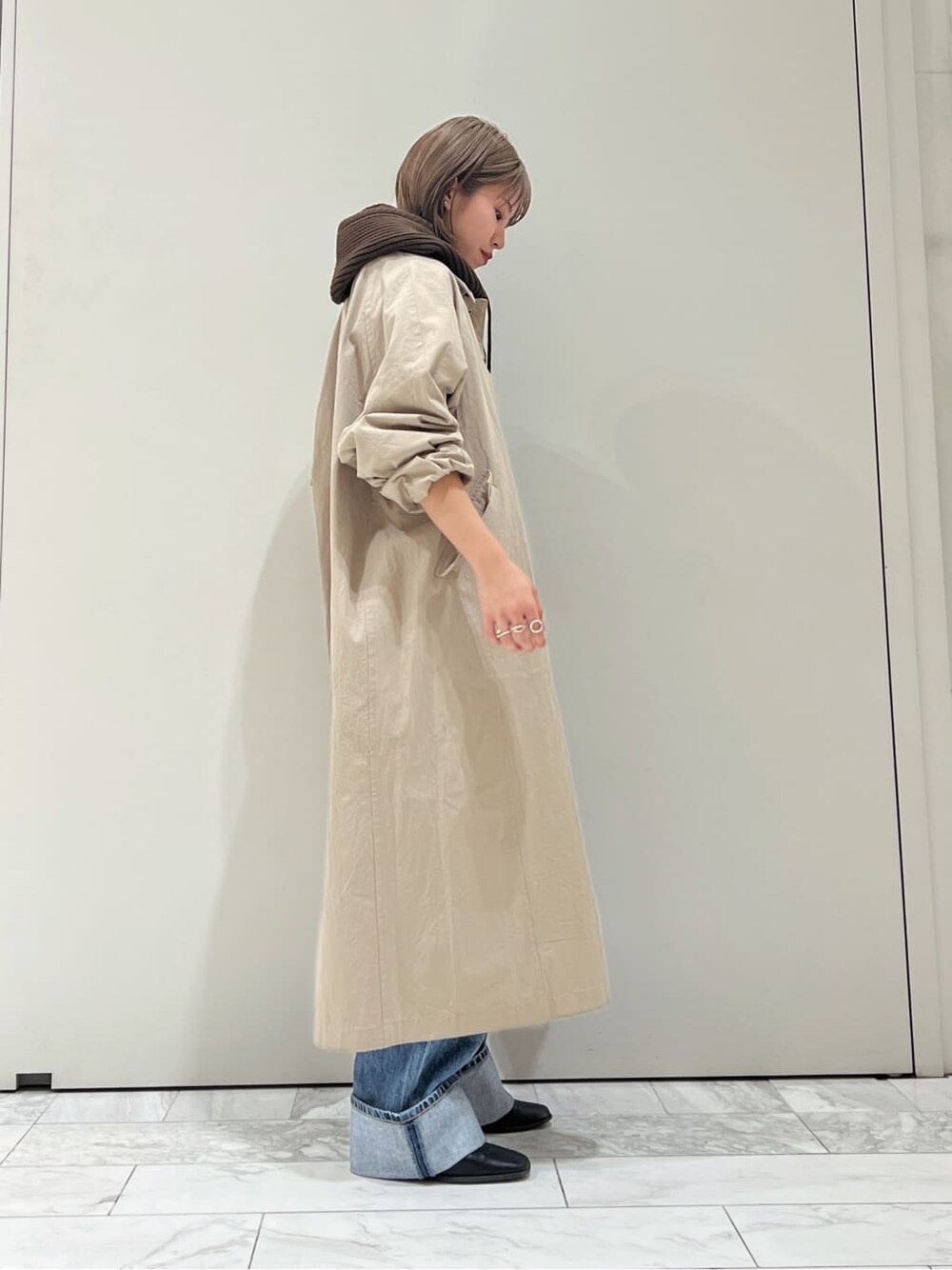 ベージュ系のステンカラーコート、ブラック系のブーツ、ブルー系のデニムパンツを着用したレディースの秋コーディネートの5枚目の写真