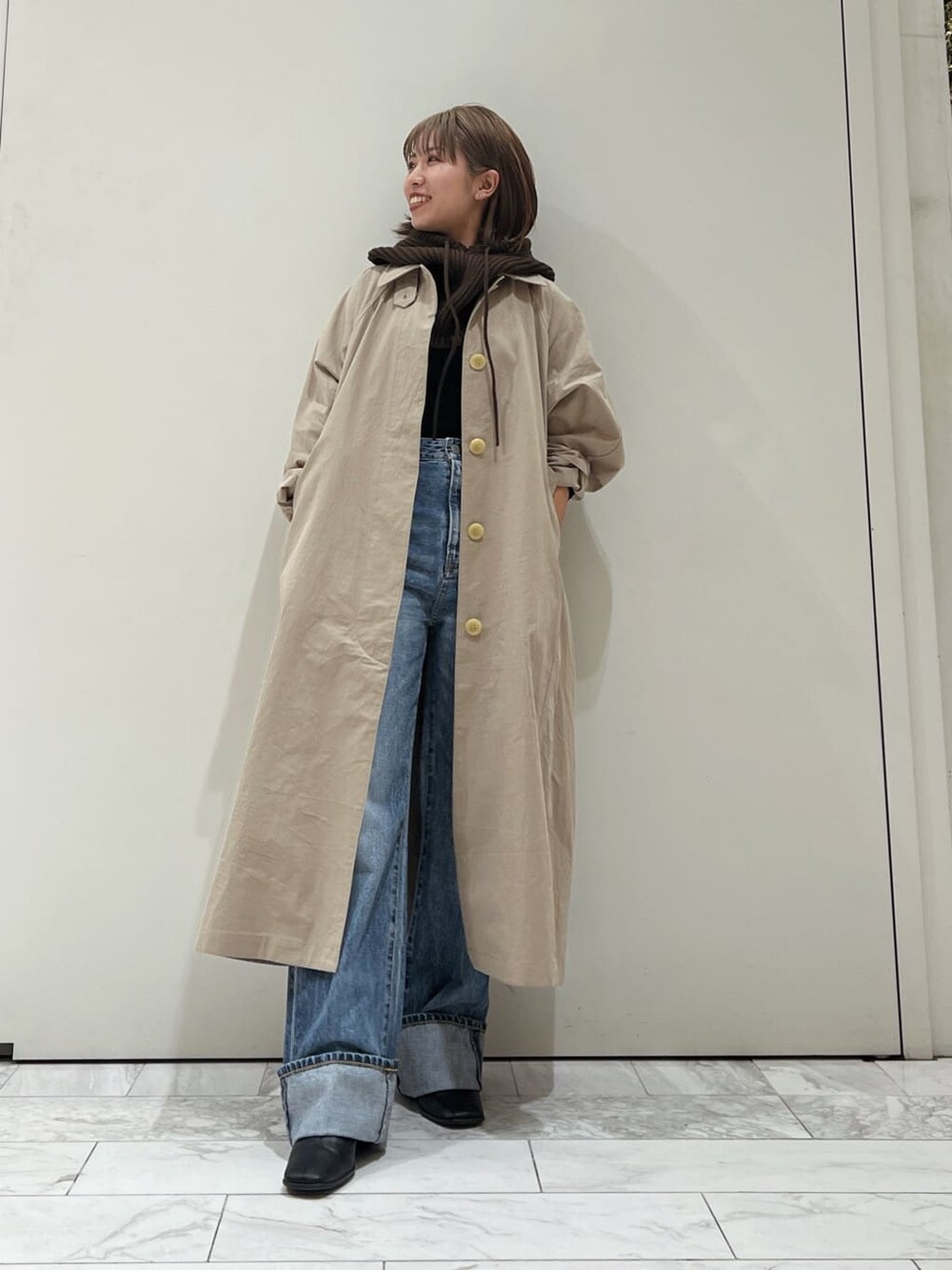 ベージュ系のステンカラーコート、ブラック系のブーツ、ブルー系のデニムパンツを着用したレディースの秋コーディネートの6枚目の写真