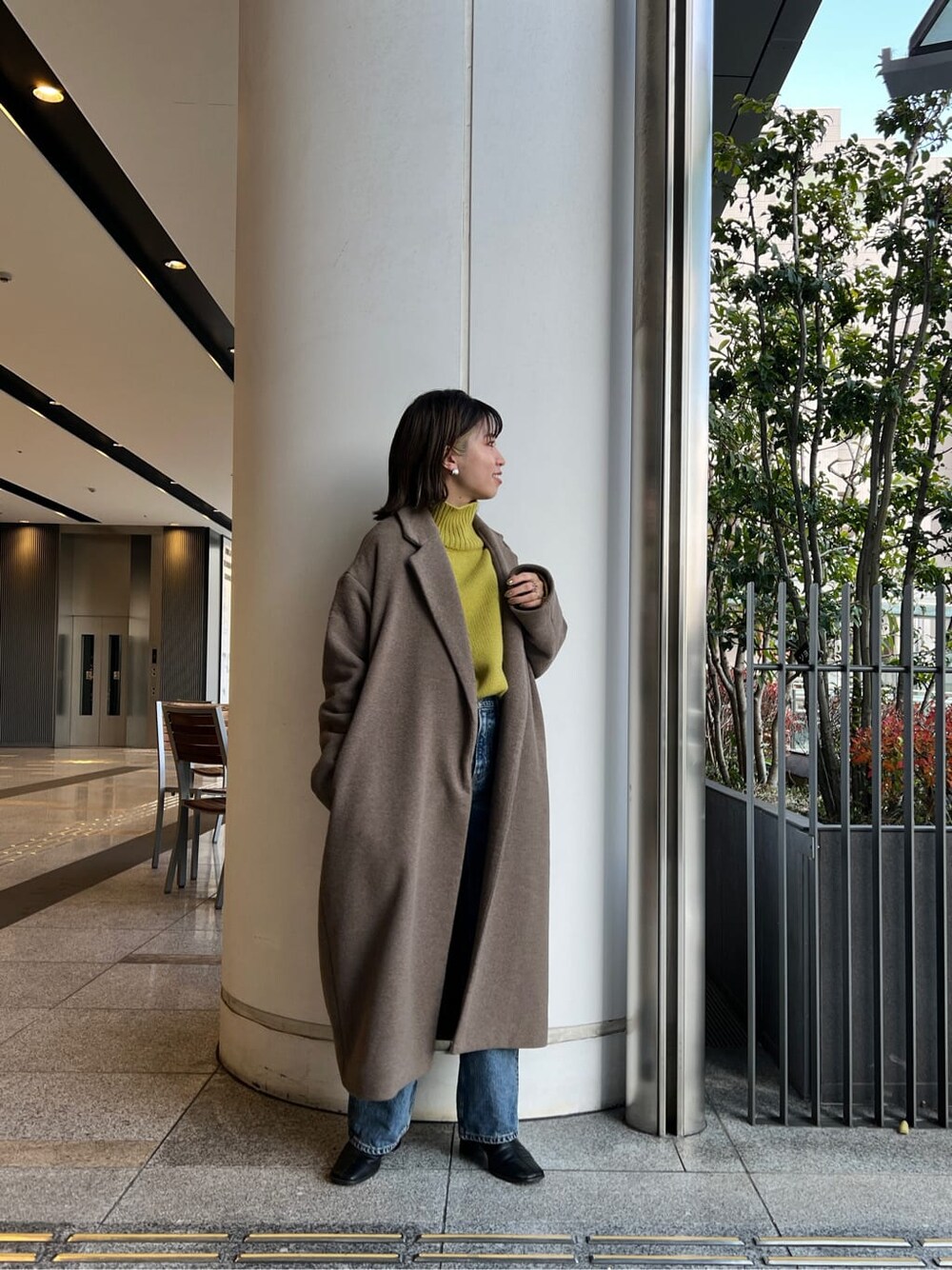 ベージュ系のチェスターコート、ブルー系のデニムパンツ、グリーン系のニット/セーターを着用したレディースの冬コーディネートの4枚目の写真