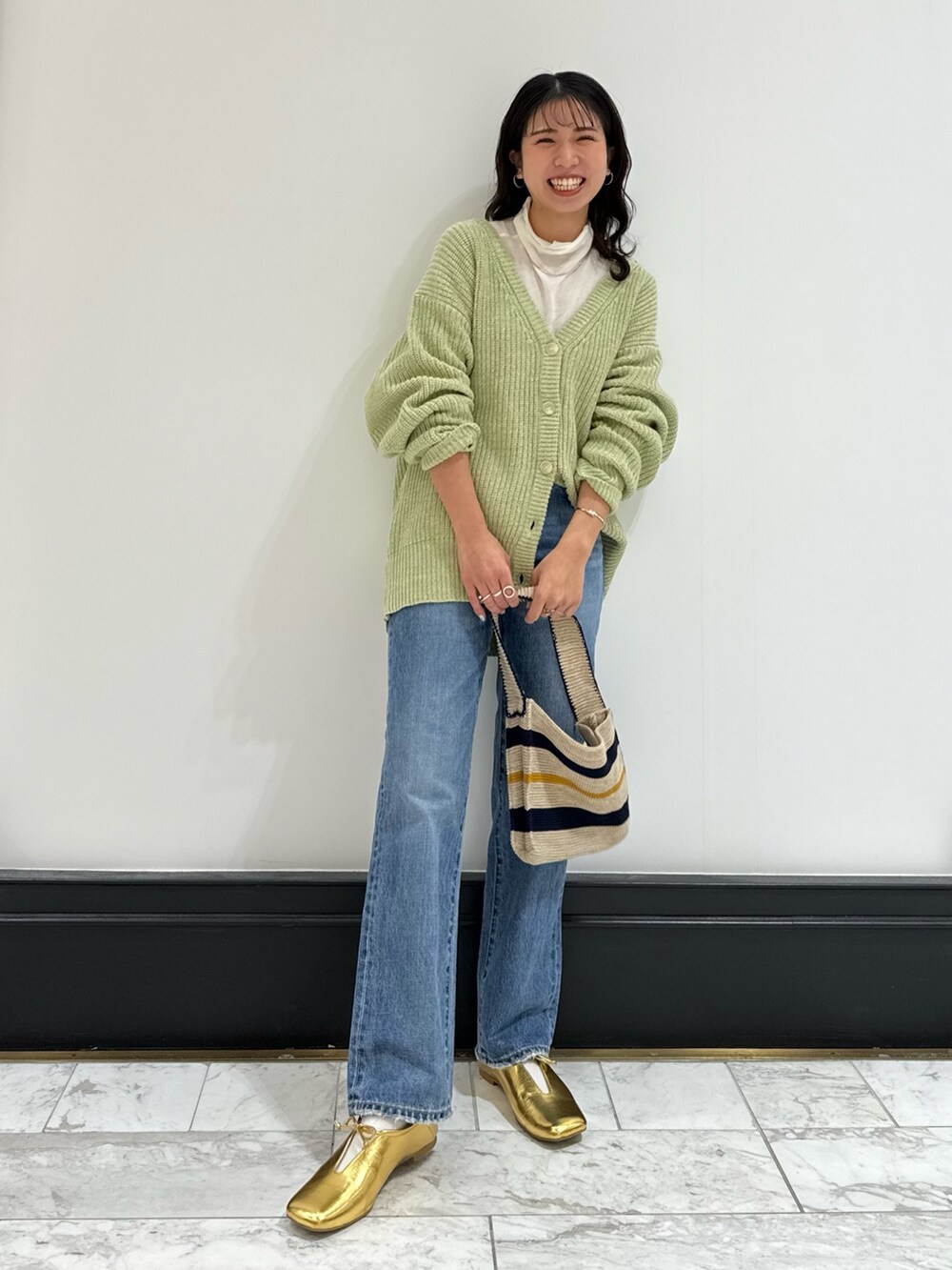グリーン系のカーディガン/ボレロ、ホワイト系のハンドバッグ、ブルー系のデニムパンツを着用したレディースの冬コーディネートの6枚目の写真
