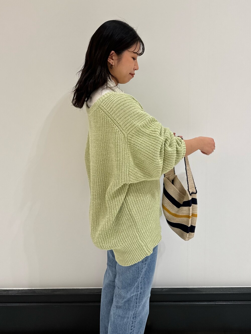 グリーン系のカーディガン/ボレロ、ホワイト系のハンドバッグ、ブルー系のデニムパンツを着用したレディースの冬コーディネートの7枚目の写真