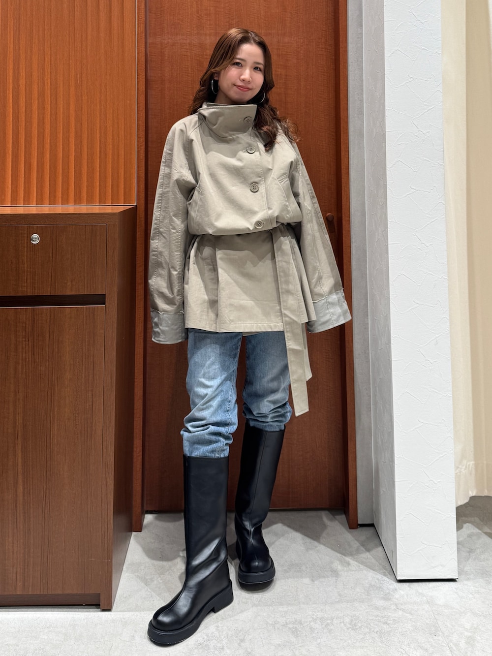 グリーン系のトレンチコート、ブルー系のデニムパンツ、ブラック系のブーツを着用したレディースの冬コーディネートの2枚目の写真