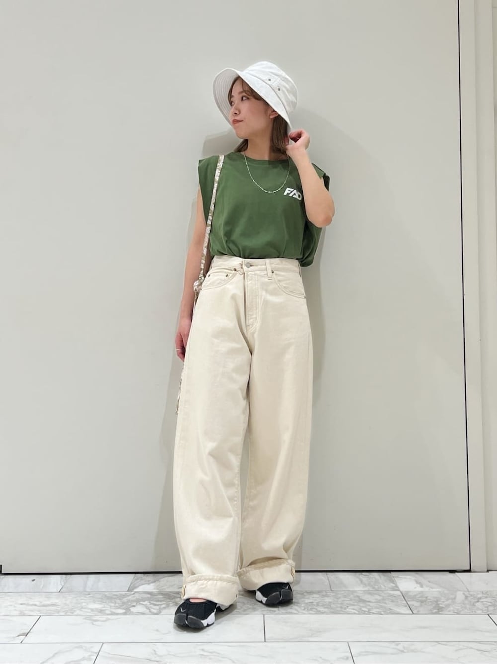 ホワイト系のデニムパンツ、グリーン系のタンクトップ、ホワイト系のハットを着用したレディースの春コーディネートの2枚目の写真