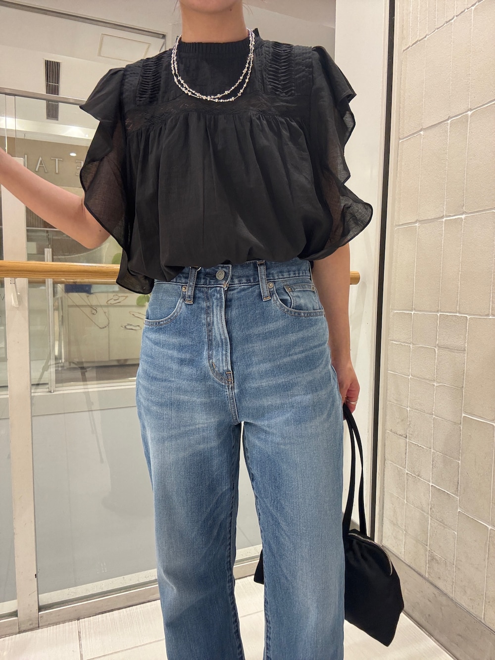 ブルー系のデニムパンツ、ブラック系のシャツ/ブラウス、ブラック系のハンドバッグを着用したレディースの春コーディネートの9枚目の写真