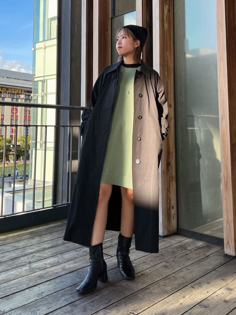 ブラック系のステンカラーコート、グリーン系のワンピース、ブラック系のブーツを着用したレディースの秋コーディネートの2枚目の写真