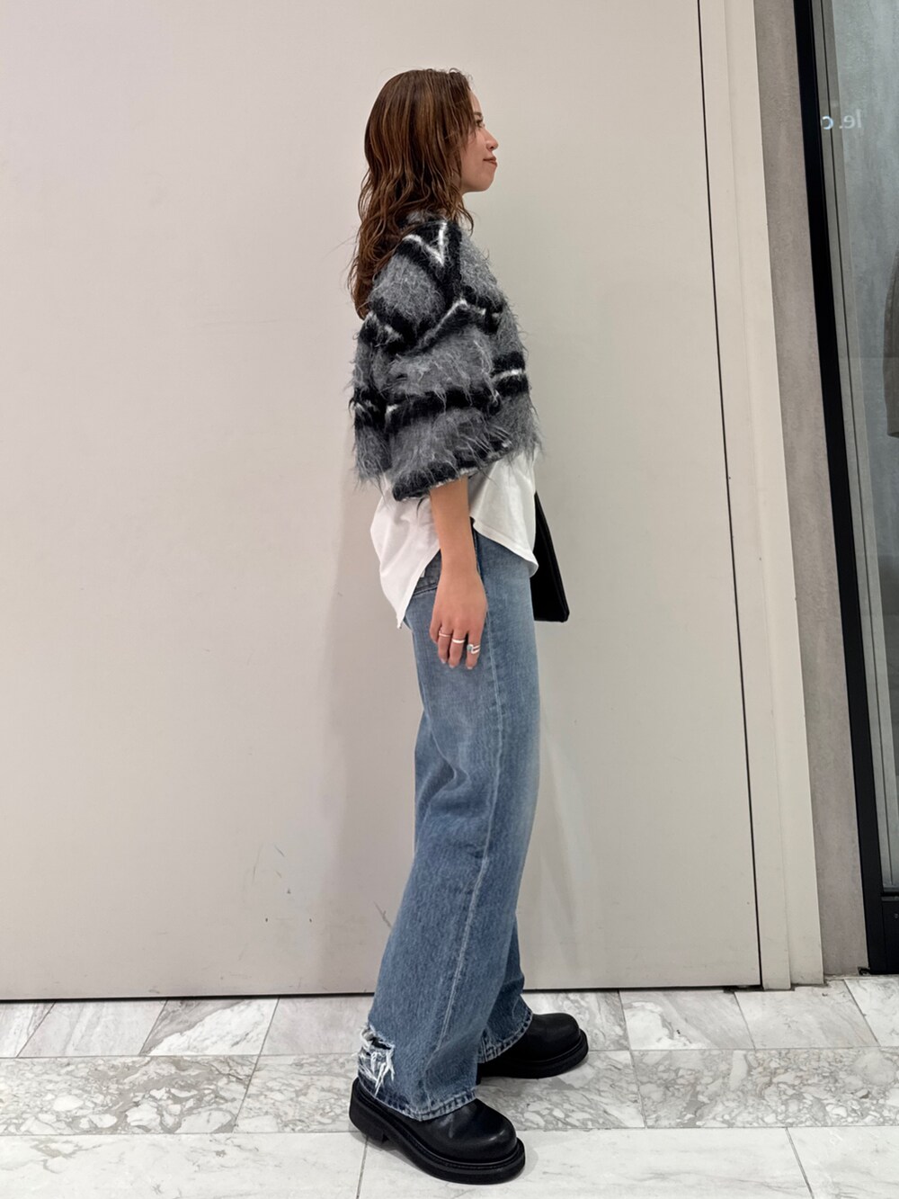 ブラック系のニット/セーター、ホワイト系のTシャツ/カットソー、ブルー系のデニムパンツを着用したレディースの冬コーディネートの3枚目の写真