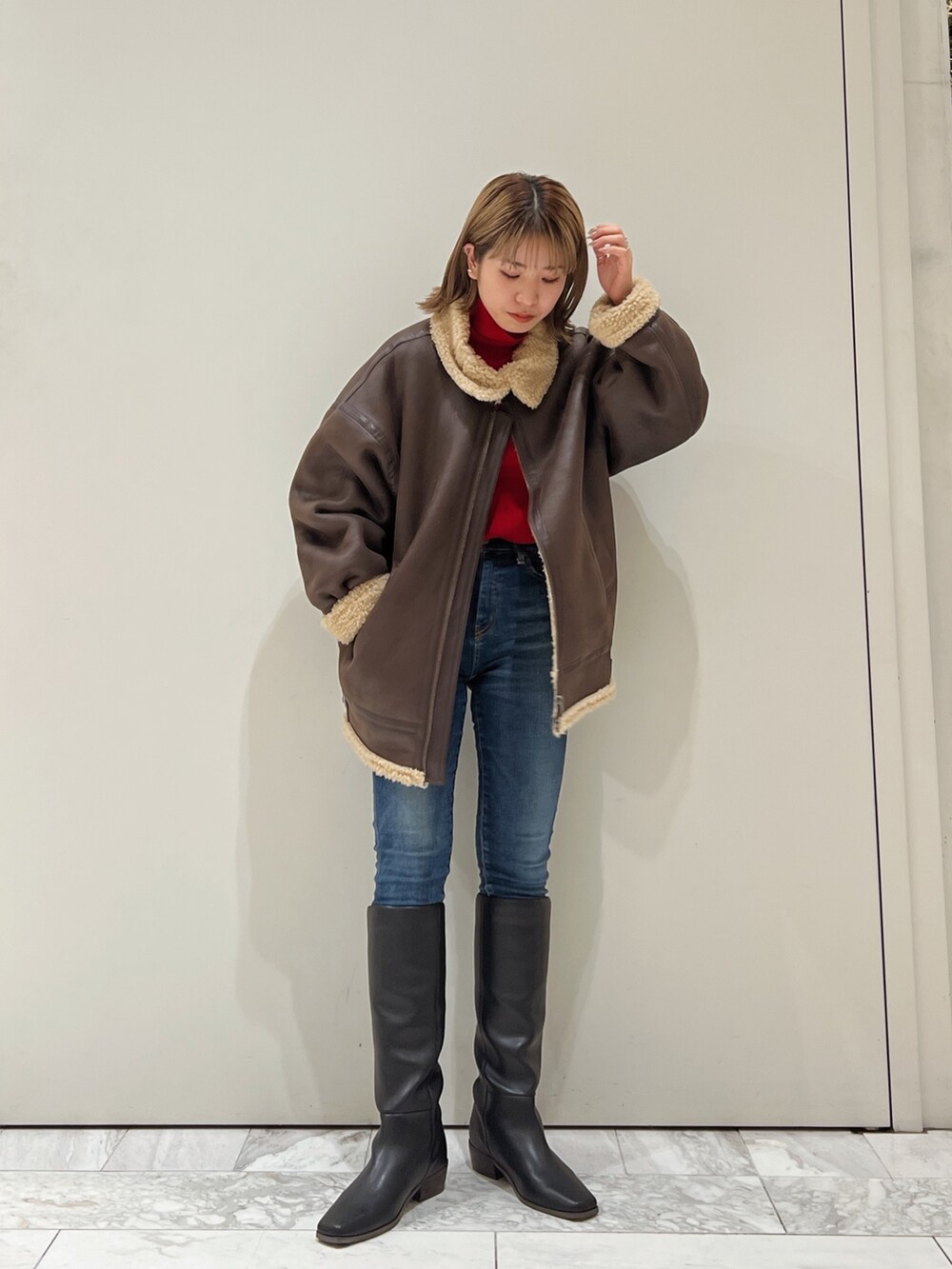 ブラウン系のムートンコート、レッド系のニット/セーター、ブルー系のデニムパンツを着用したレディースの冬コーディネートの2枚目の写真