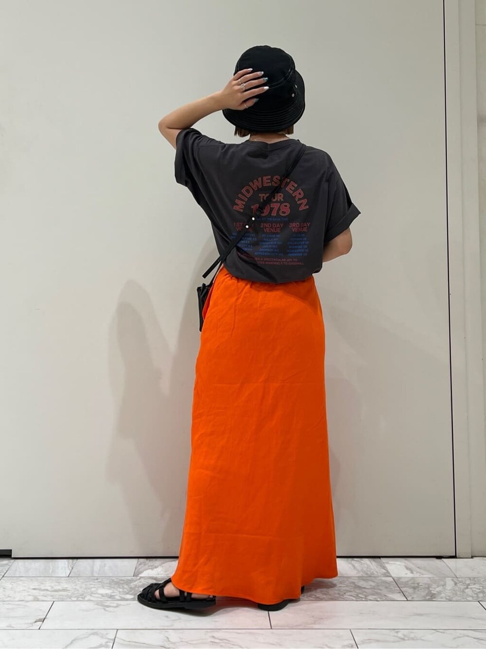 ブラック系のショルダーバッグ、グレー系のTシャツ/カットソー、オレンジ系のスカートを着用したレディースの夏コーディネートの3枚目の写真