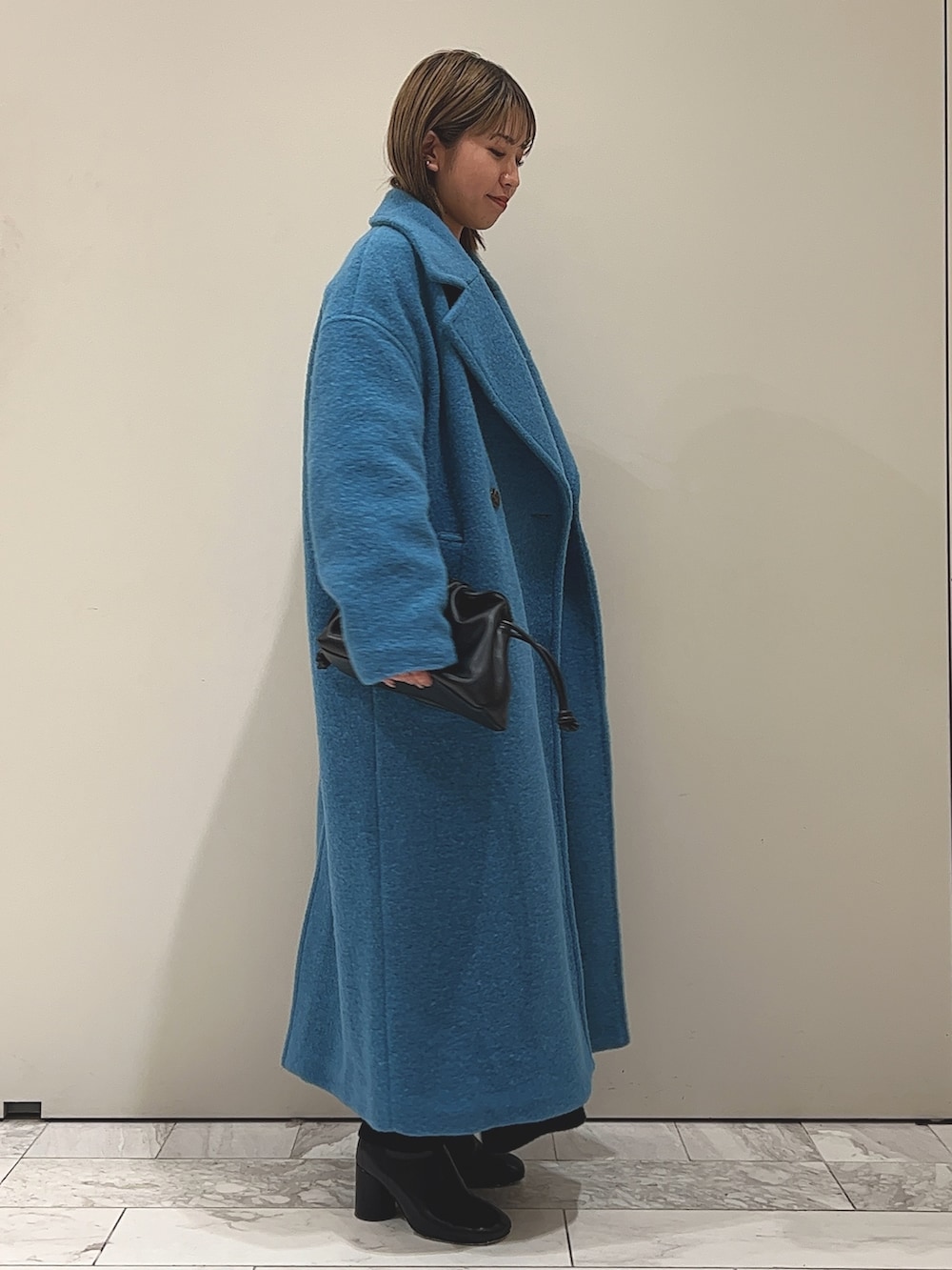 ブルー系のチェスターコート、ブラック系のワンピース、ブラック系のブーツを着用したレディースの冬コーディネートの2枚目の写真