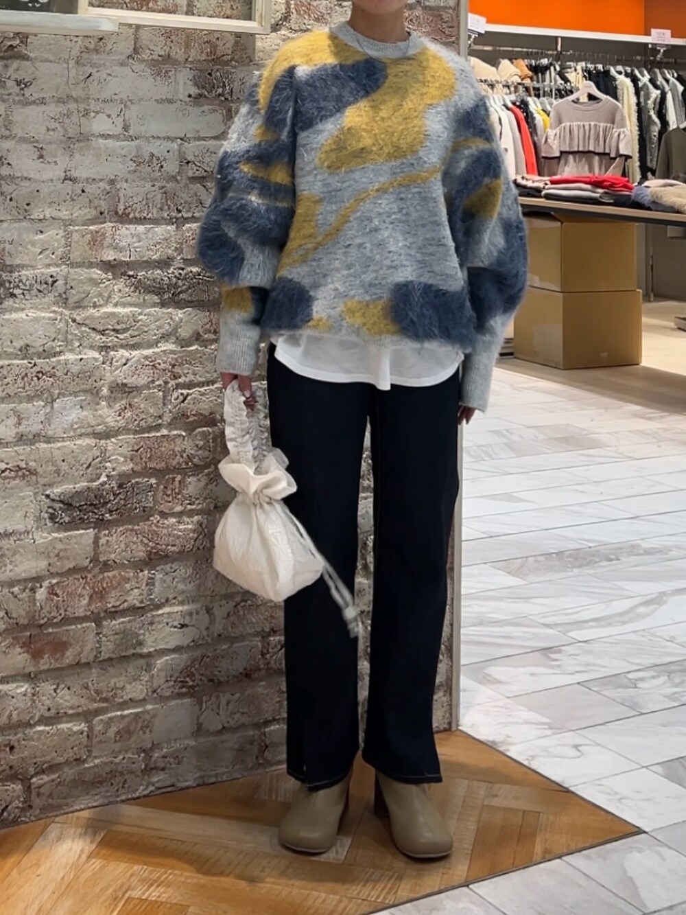 ブルー系のニット/セーター、ホワイト系のハンドバッグ、ブルー系のデニムパンツを着用したレディースの秋コーディネートの5枚目の写真