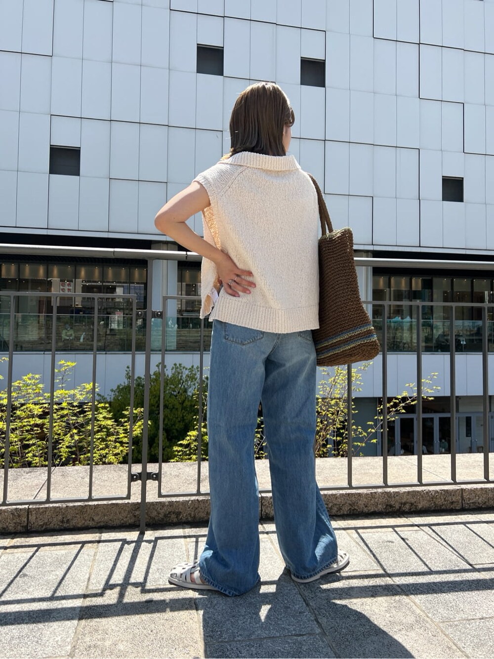 ブラウン系のトートバッグ、ブルー系のデニムパンツ、ホワイト系のサンダルを着用したレディースの春コーディネートの2枚目の写真