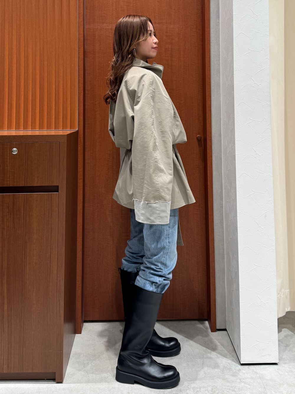 グリーン系のトレンチコート、ブルー系のデニムパンツ、ブラック系のブーツを着用したレディースの冬コーディネートの3枚目の写真