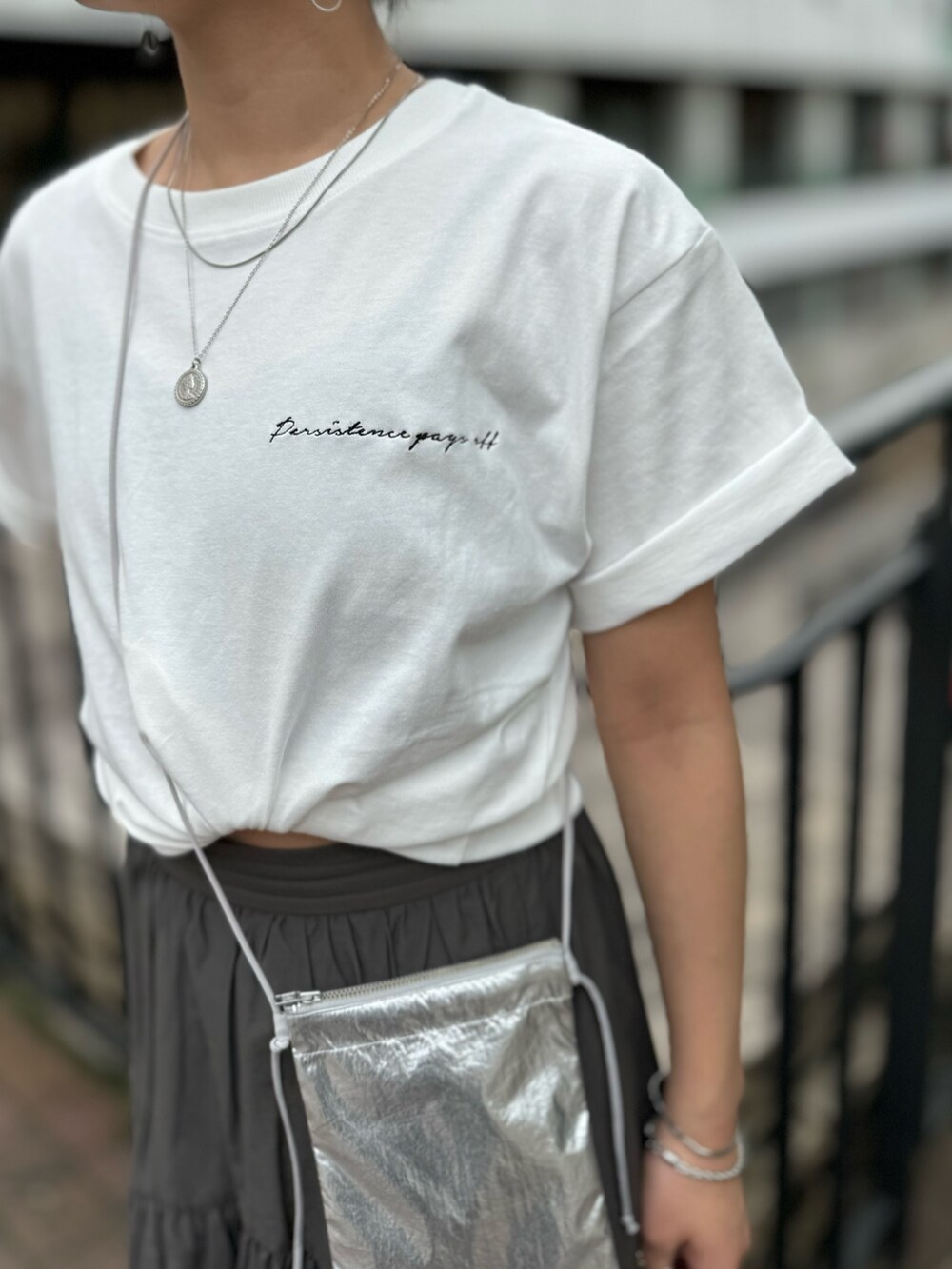 シルバー系のショルダーバッグ、ホワイト系のTシャツ/カットソー、グレー系のスカートを着用したレディースの春コーディネートの9枚目の写真