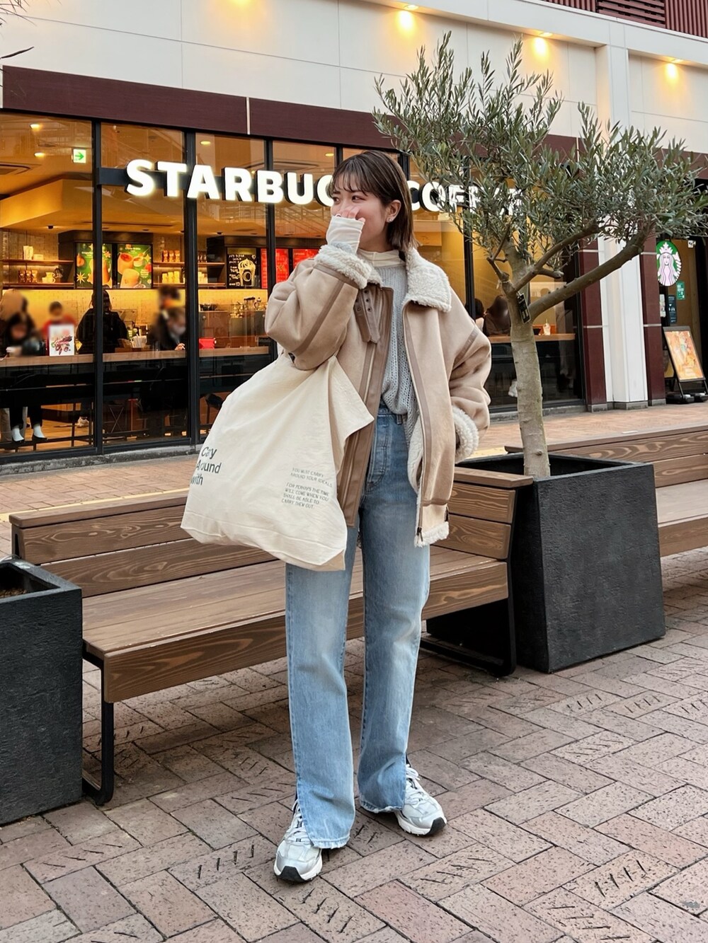 ベージュ系のムートンコート、ホワイト系のハンドバッグ、グレー系のニット/セーターを着用したレディースの冬コーディネートの4枚目の写真