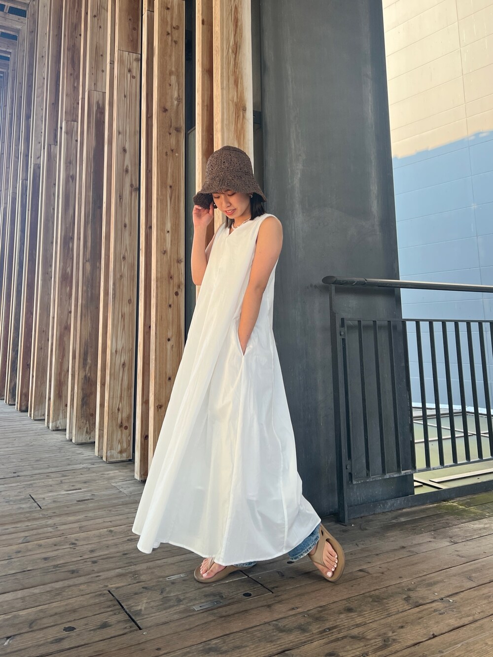 ホワイト系のワンピース、ブルー系のデニムパンツ、ブラウン系のハットを着用したレディースの夏コーディネートの2枚目の写真