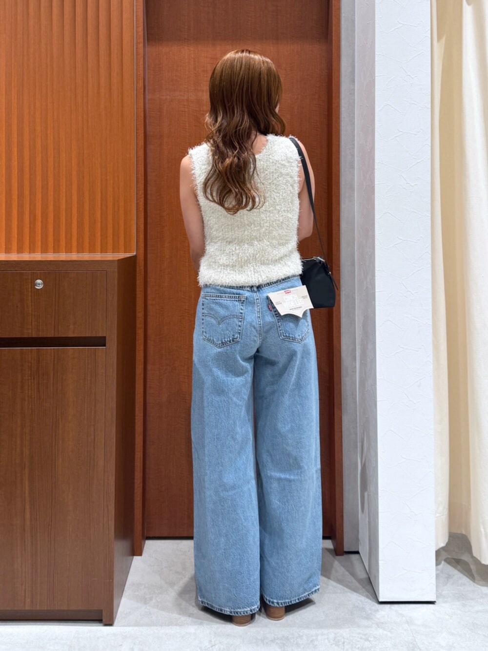 ブルー系のデニムパンツ、ホワイト系のベスト、ブラック系のハンドバッグを着用したレディースの夏コーディネートの4枚目の写真