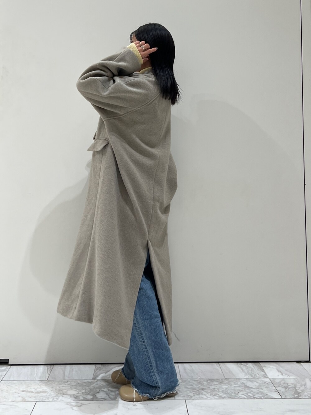 グレー系のチェスターコート、イエロー系のニット/セーター、ブルー系のデニムパンツを着用したレディースの秋コーディネートの9枚目の写真