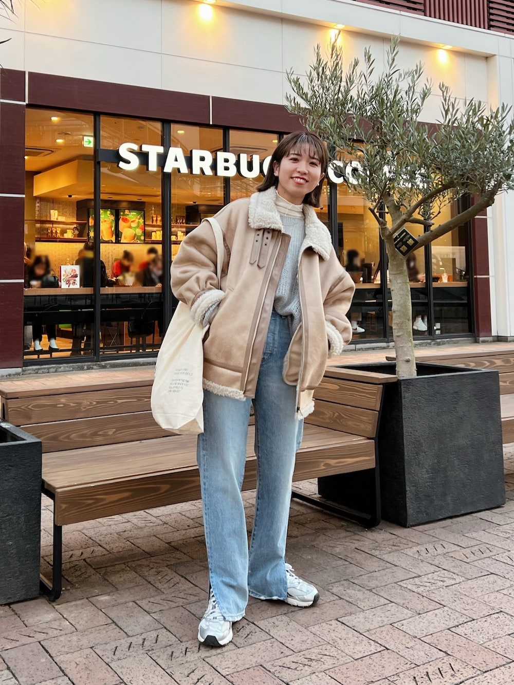 ベージュ系のムートンコート、ホワイト系のハンドバッグ、グレー系のニット/セーターを着用したレディースの冬コーディネートの6枚目の写真