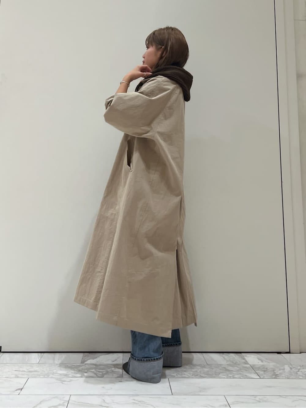 ベージュ系のステンカラーコート、ブラック系のブーツ、ブルー系のデニムパンツを着用したレディースの秋コーディネートの3枚目の写真