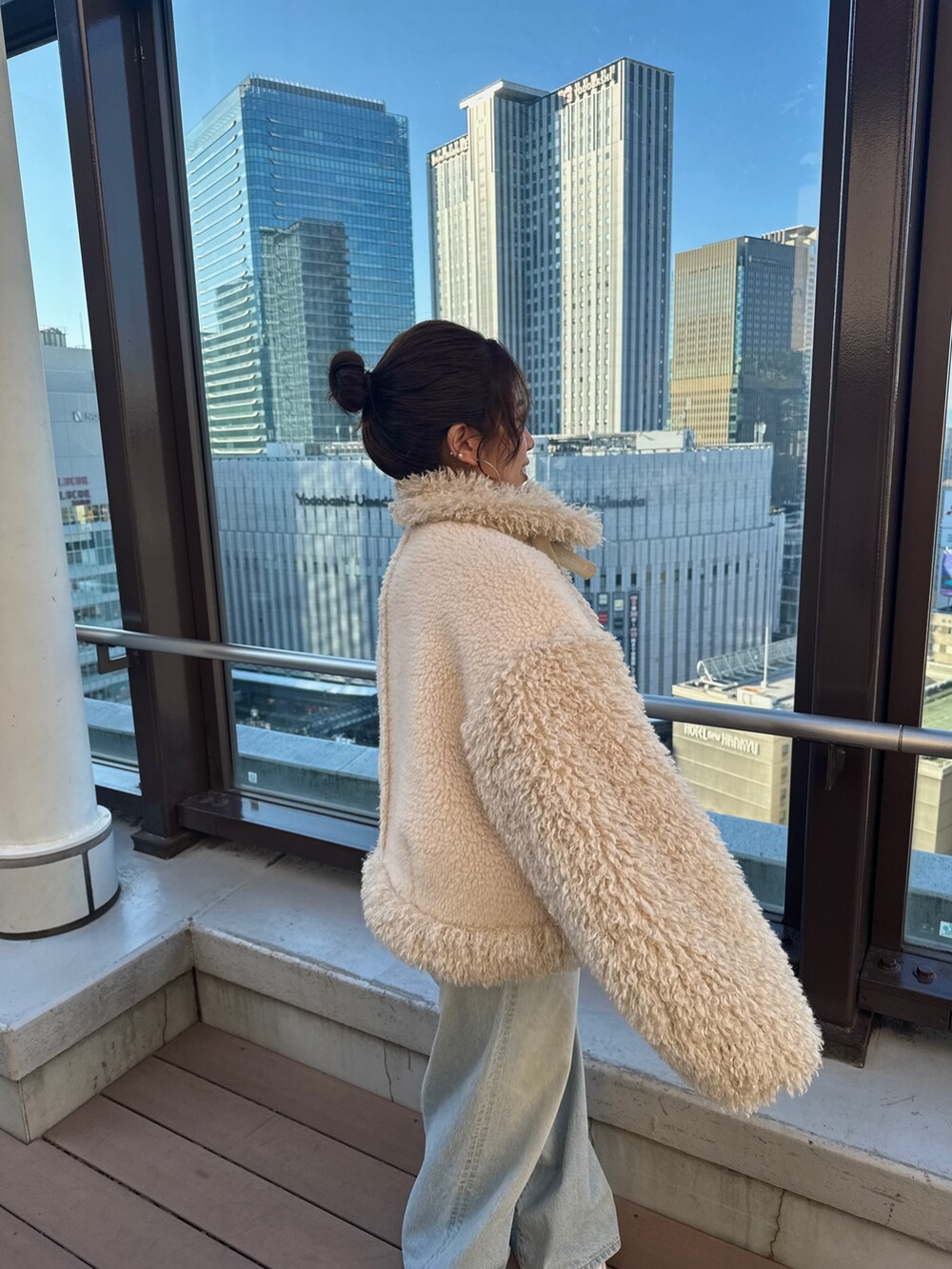 ホワイト系のムートンコート、グリーン系のニット/セーター、ブルー系のデニムパンツを着用したレディースの冬コーディネートの6枚目の写真