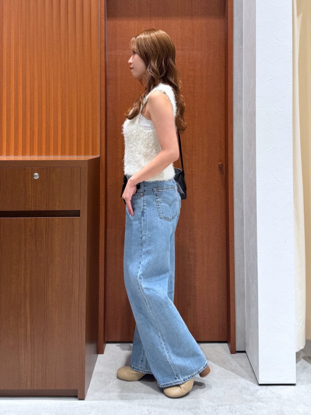 ブルー系のデニムパンツ、ホワイト系のベスト、ブラック系のハンドバッグを着用したレディースの夏コーディネートの5枚目の写真