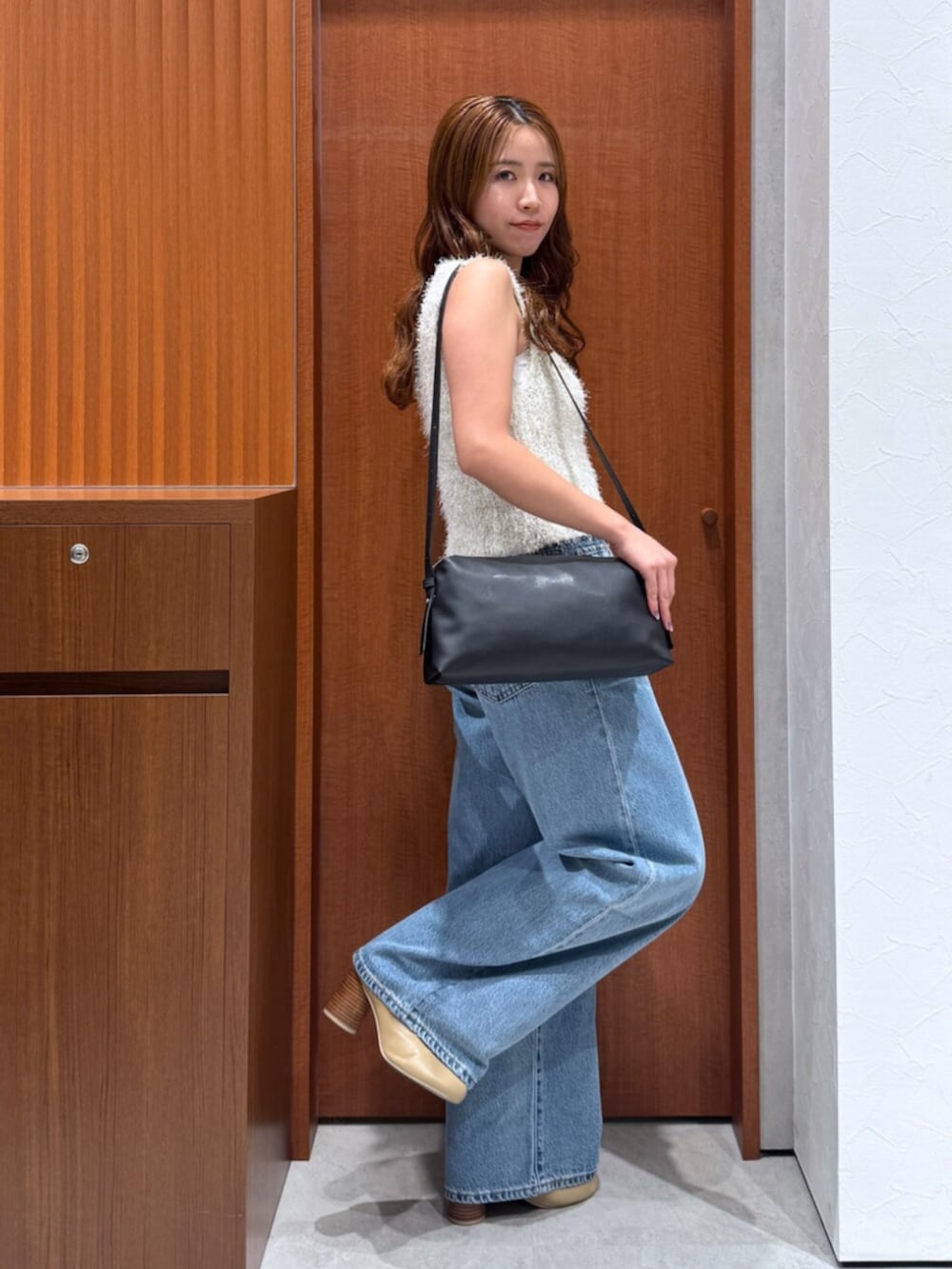 ブルー系のデニムパンツ、ホワイト系のベスト、ブラック系のハンドバッグを着用したレディースの夏コーディネートの3枚目の写真