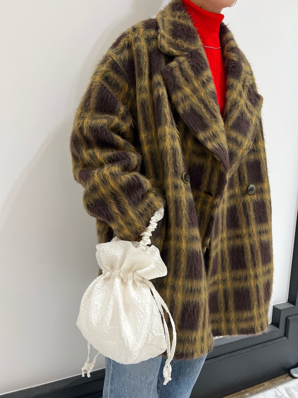 レッド系のニット/セーター、ホワイト系のハンドバッグ、ブルー系のデニムパンツを着用したレディースの冬コーディネートの5枚目の写真