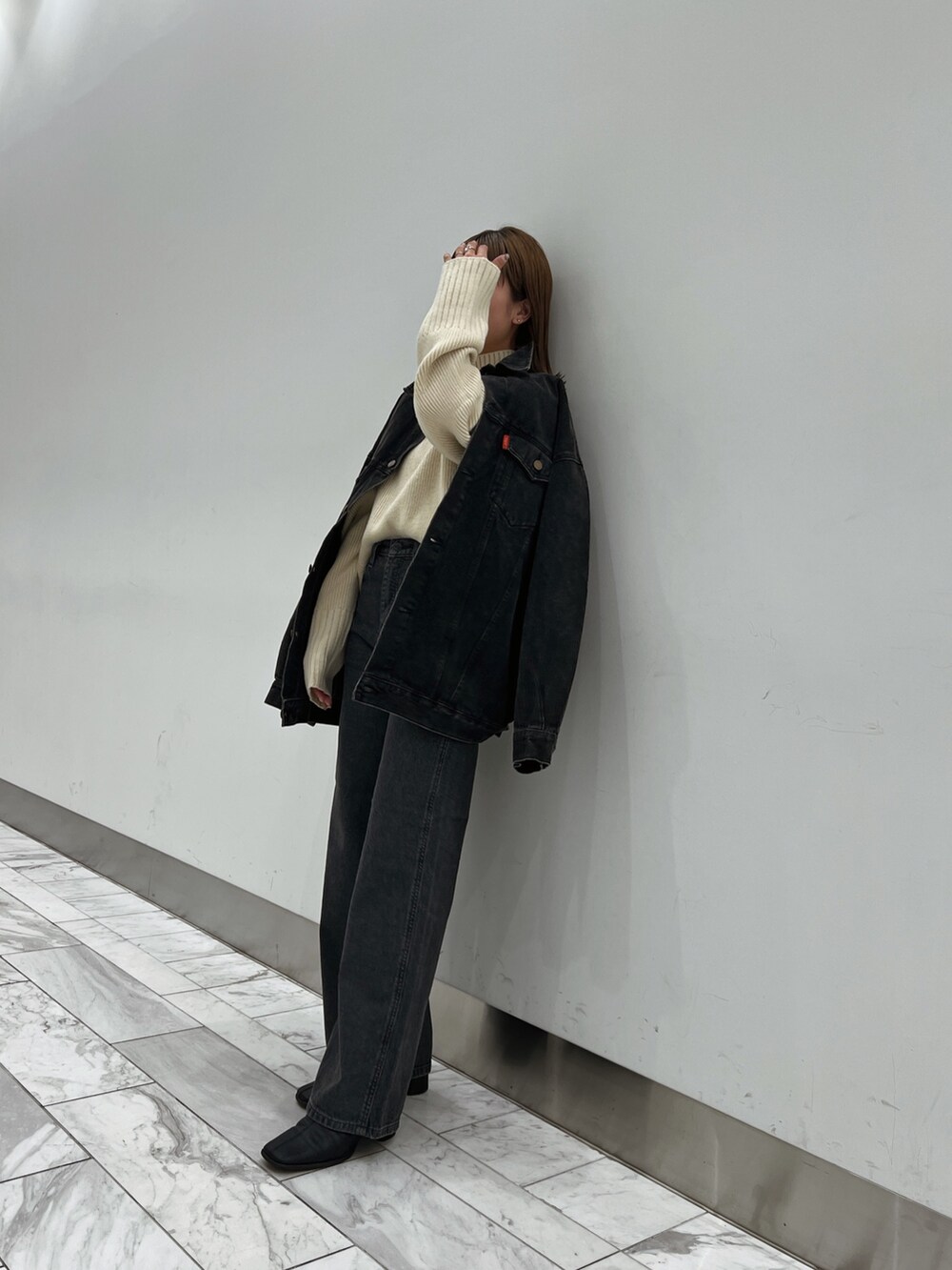 ブラック系のデニムジャケット、ホワイト系のニット/セーター、ブラック系のデニムパンツを着用したレディースの秋コーディネートの2枚目の写真