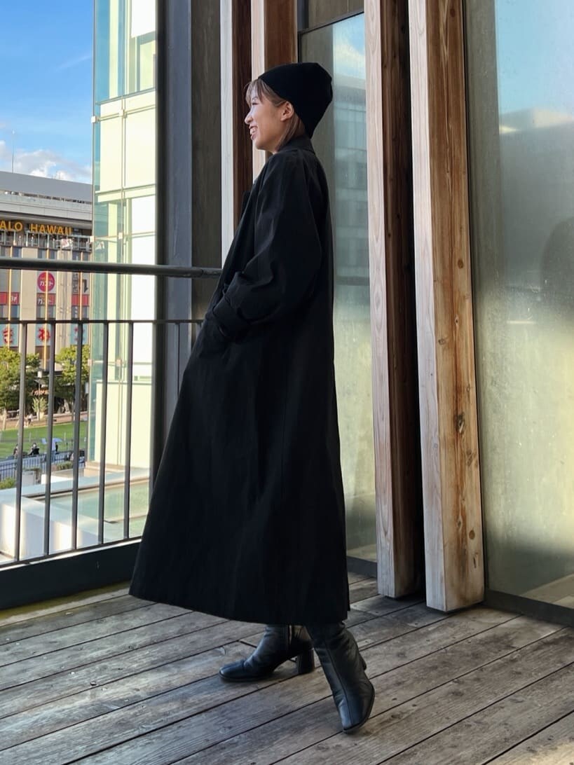 ブラック系のステンカラーコート、グリーン系のワンピース、ブラック系のブーツを着用したレディースの秋コーディネートの3枚目の写真