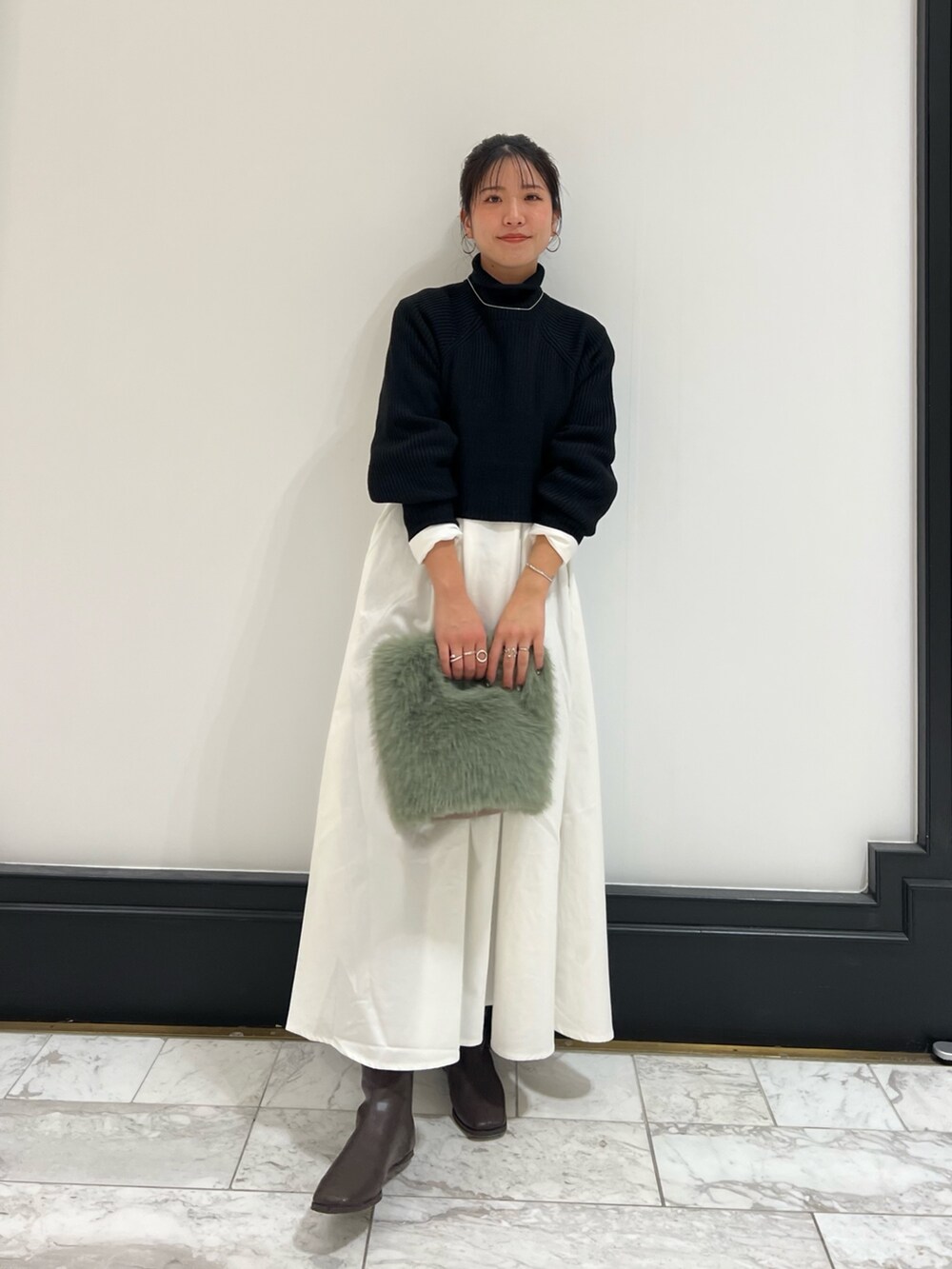 ブラック系のワンピース、グリーン系のハンドバッグ、ブラウン系のブーツを着用したレディースの冬コーディネートの7枚目の写真