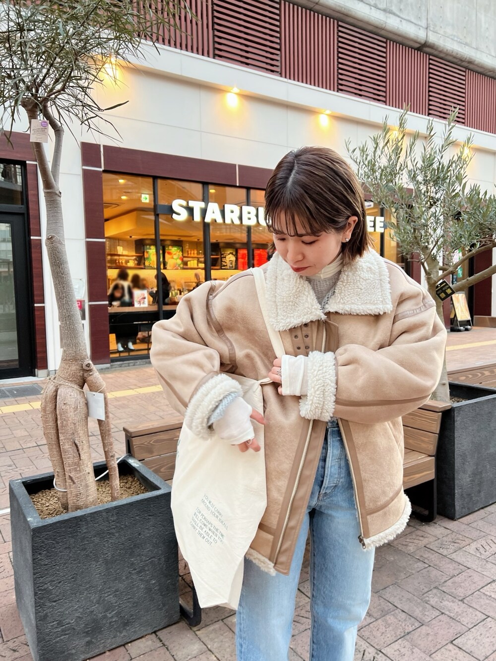 ベージュ系のムートンコート、ホワイト系のハンドバッグ、グレー系のニット/セーターを着用したレディースの冬コーディネートの3枚目の写真